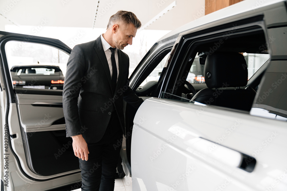 Mature white man choosing and examining car in showroom