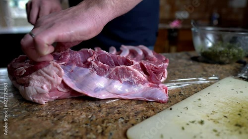 Man prepares a large piece of pork pelly for roasting. Adds herb and spices rub to marinate the meat. Home cooking concept. photo