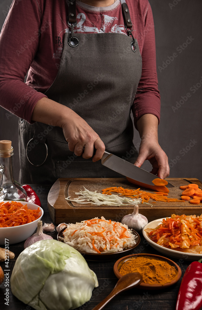 Home cooking. A kitchen table where a woman slices vegetables on a wooden board for fermentation and salting. Vertical orientation, no face