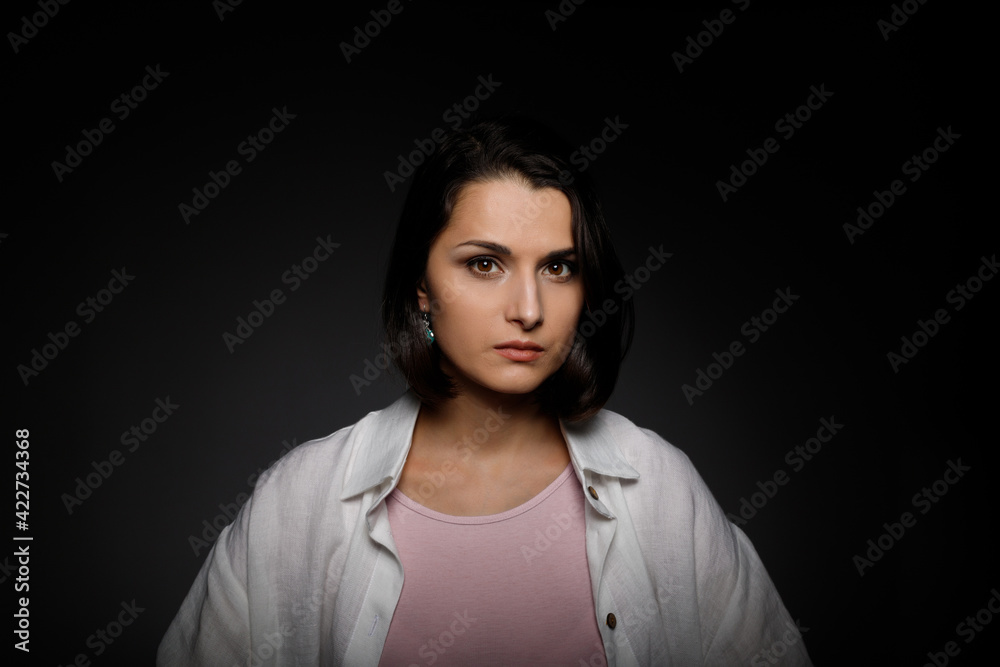 Low key portrait of serious young brunette multiethnic woman in pink tank and white shirt looking at camera Low key portrait of serious young brunette multiethnic woman in pink tank and white shirt looking at camera