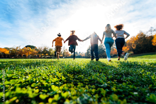 Group of multiracial people holding hands running in the park - Happy friends having fun together outdoor on sunset - People and community concept