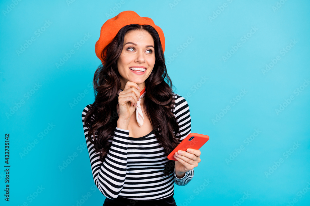 Photo of young girl happy smile hand touch chin think dream look empty space use smartphone isolated over blue color background Photo of young girl happy smile hand touch chin think dream look empty space use smartphone isolated over blue color background
