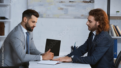 young businessmen in formal wear talking near laptop in office