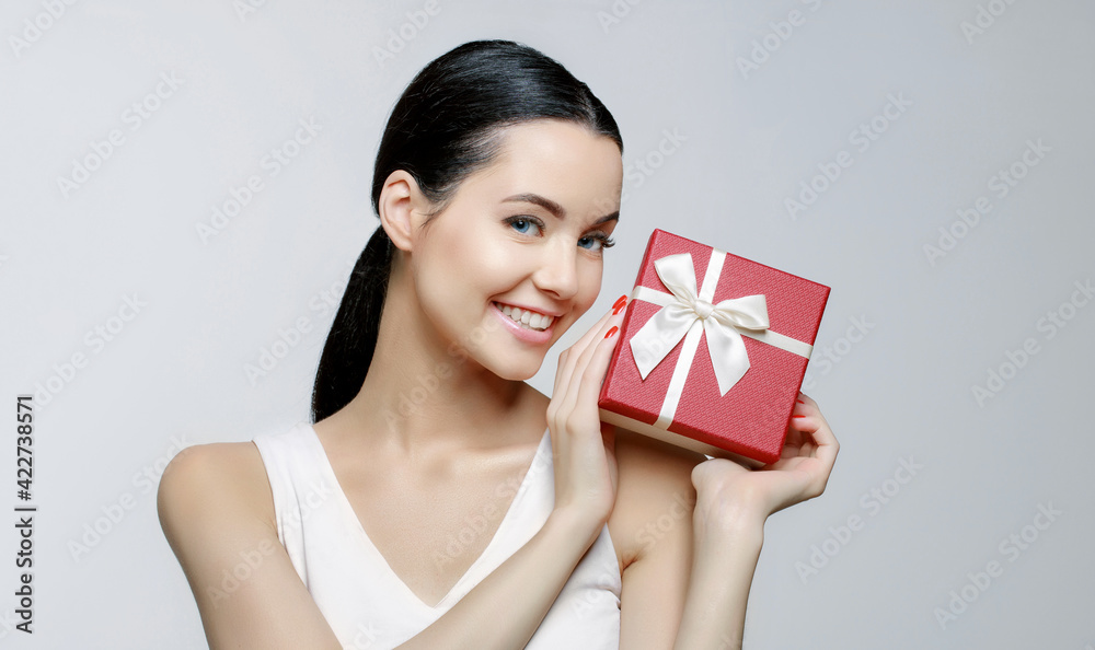 Cheerful woman holding present box in studio on gray background. Smiling beautiful young girl expressing happy emotions. Seasonal discounts and sale. Cheerful woman holding present box in studio on gray background. Smiling beautiful young girl expressing happy emotions. Seasonal discounts and sale.