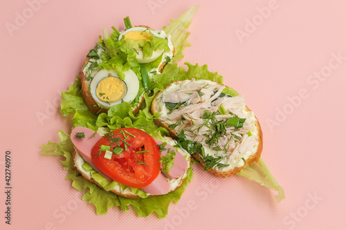 Three sandwiches with egg, sausage, chicken and parsley lie on a pink background