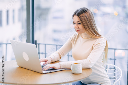 Young freelancer woman uses a laptop, at a cafe table. Serious w Free Download Young freelancer woman uses a laptop, at a cafe table. Serious w - GFXLoad
