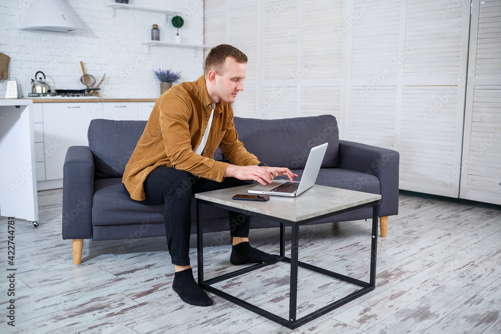 Young successful man is sitting at home on the couch with a laptop and working. Remote work during quarantine. Young successful man is sitting at home on the couch with a laptop and working. Remote work during quarantine.