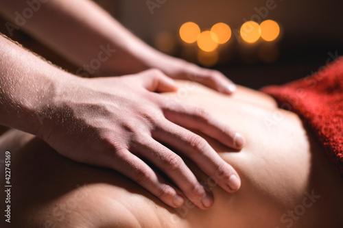 Massage of a female back in a dark room of a spa salon. Male masseur doing massage of the back of the body and lower back © yanik88