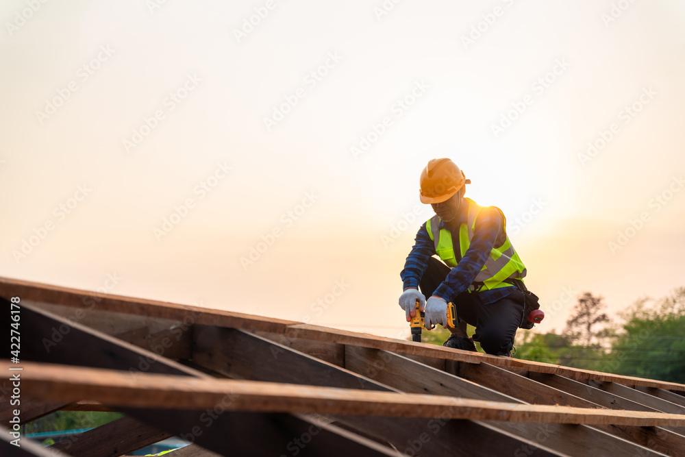 Asian roofer working on roof structure of building on construction site, Roofer using air or pneumatic nail gun and installing on wooden roof structure. Asian roofer working on roof structure of building on construction site, Roofer using air or pneumatic nail gun and installing on wooden roof structure.