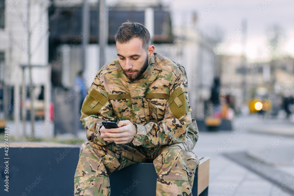 A military soldier sits on a bench at a bus stop waiting for a b A military soldier sits on a bench at a bus stop waiting for a b