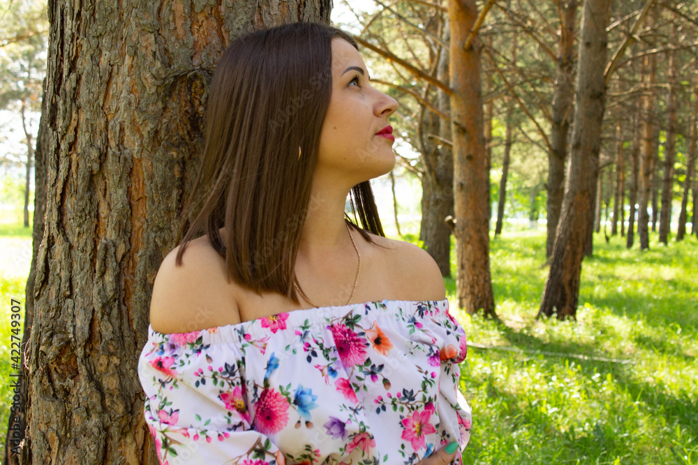 Beautiful sexy girl with short hair in dress stands near a tree in the pine forest Beautiful sexy girl with short hair in dress stands near a tree in the pine forest