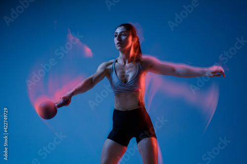 Caucasian professional female athlete training on blue studio background in neon  mixed light. Muscular  sportive woman.