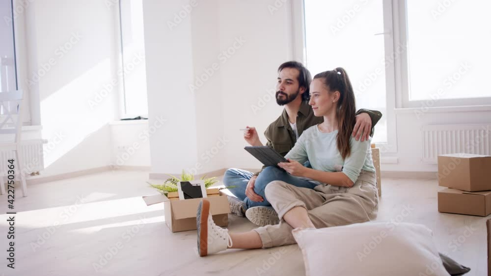 Side view of young couple with tablet moving and planning in new flat, new home and relocation concept. Side view of young couple with tablet moving and planning in new flat, new home and relocation concept.