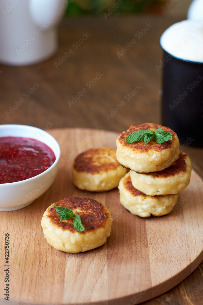 Syrnik with raspberry jam, coffee, mint. Side view, wooden background.Cheesecakes with raspberry jam, coffee, mint. Side view, wooden background. cheese pancake Syrnik with raspberry jam, coffee, mint. Side view, wooden background.Cheesecakes with raspberry jam, coffee, mint. Side view, wooden background. cheese pancake