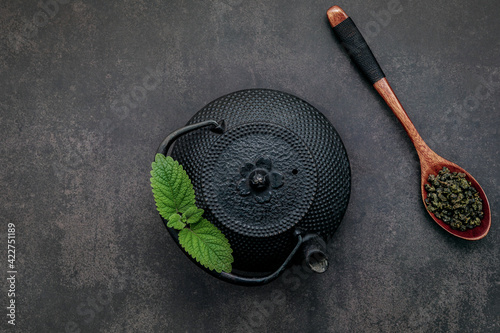  Black cast iron tea pot with herbal tea set up on dark stone background.