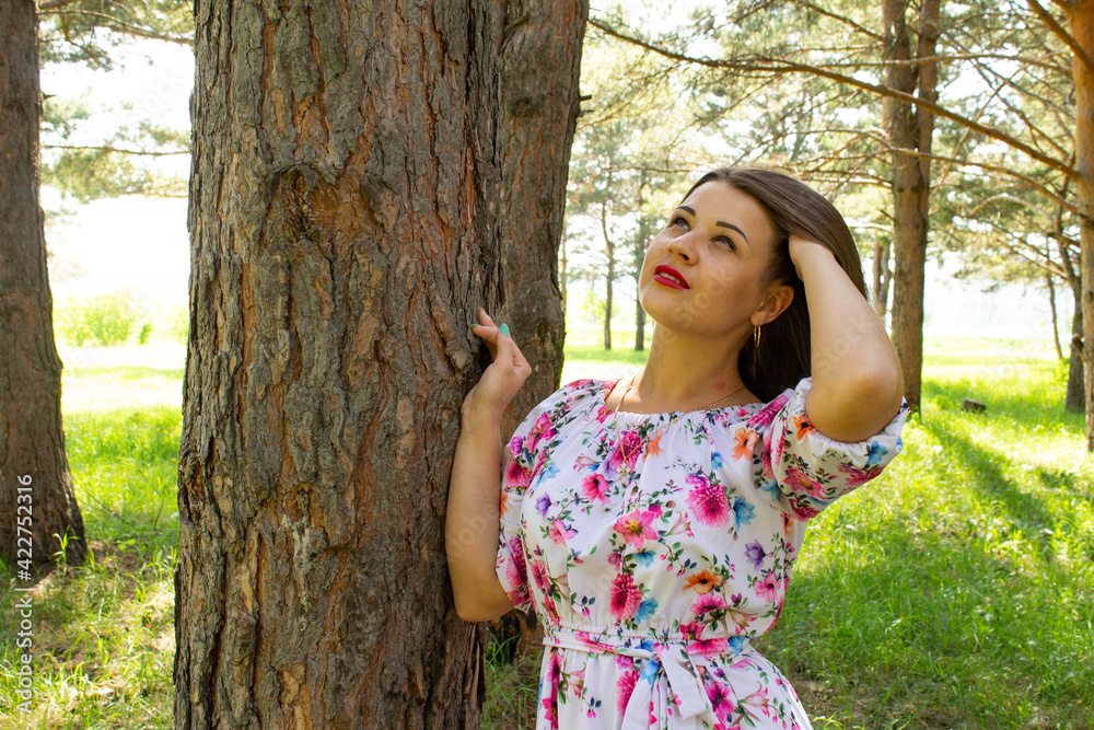 Beautiful sexy girl with short hair in dress stands near a tree in the pine forest Beautiful sexy girl with short hair in dress stands near a tree in the pine forest