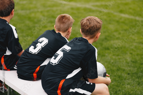 Young School Boys in a Sports Team Sitting on Substitute Bench. Kids on Football Game. Young Boy Holding Soccer Ball. Group of Children Athletes Watching Match