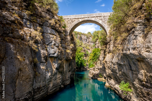 Ancient arch bridge Oluk over the Koprucay river gorge in Koprulu national Park in Turkey. Panoramic scenic view of the canyon and blue stormy mountain river