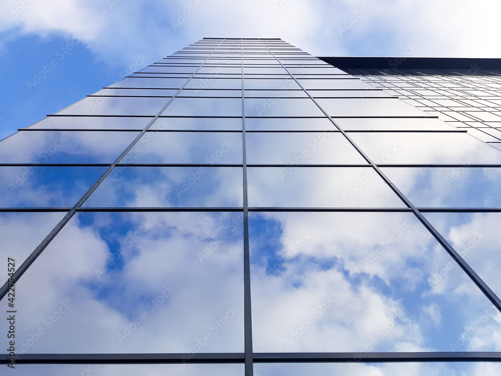 View of a modern glass skyscraper. Reflection of a cloudy blue sky in a glass skyscraper View of a modern glass skyscraper. Reflection of a cloudy blue sky in a glass skyscraper