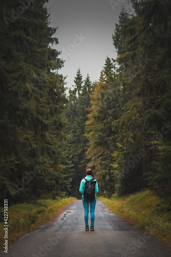 girl in sportswear and a tourist with a backpack stands motionless on a forest path between two different forests in the Jizera Mountains. Woman on a hike. A walk through the Czech wilderness