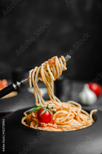 Pasta with feta cheese and baked tomatoes in a black plate. Spaghetti