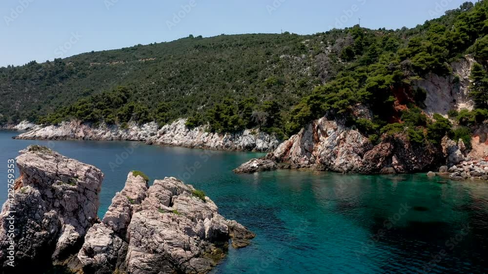Aerial drone views over a rocky coastline, crystal clear Aegean sea waters, touristic beaches and lots of greenery in Skopelos island, Greece. A typical view of many similar Greek islands. Aerial drone views over a rocky coastline, crystal clear Aegean sea waters, touristic beaches and lots of greenery in Skopelos island, Greece. A typical view of many similar Greek islands.
