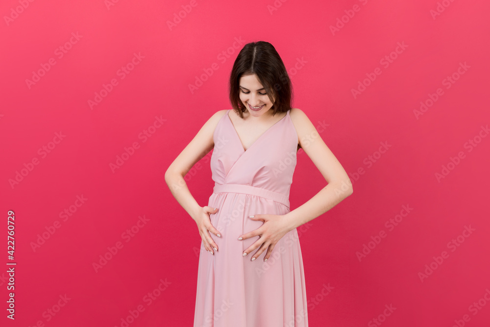 Happy pregnant woman touching her abdomen at Colored background. Future mother. Expecting of a baby. Copy space Happy pregnant woman touching her abdomen at Colored background. Future mother. Expecting of a baby. Copy space