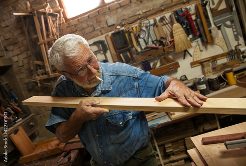 Experienced senior carpenter in his workshop. Measuring the wooden furniture part . 