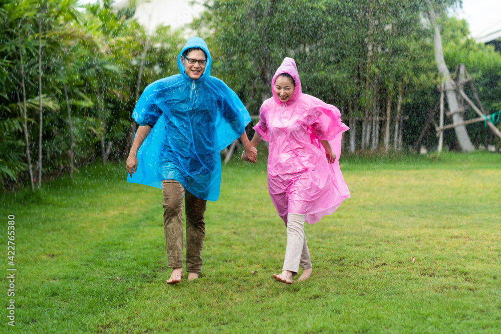 Obraz premium Happy Asian couple wearing a raincoat play in the rain outdoors at park.