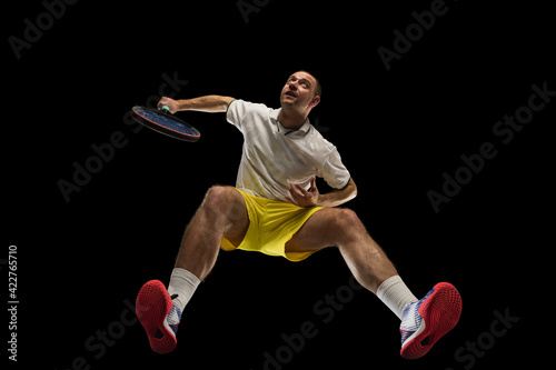Young caucasian tennis player in action, motion isolated on black background, look from the bottom. Concept of sport, movement, energy and dynamic.
