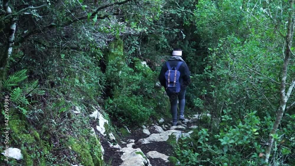 Girl with a backpack walking down on a rock path in nature surrounded by beautiful green leaves trees. Girl with a backpack walking down on a rock path in nature surrounded by beautiful green leaves trees.