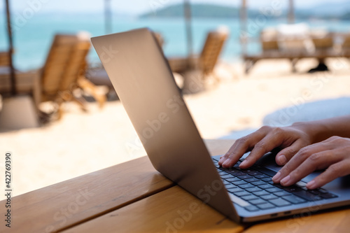 Closeup of a woman working and typing on laptop computer on the beach