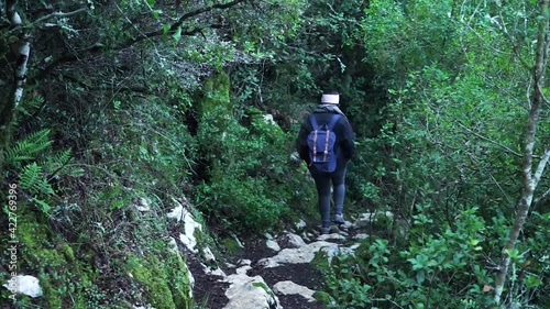 Girl with a backpack walking down on a rock path in nature surrounded by beautiful green leaves trees.