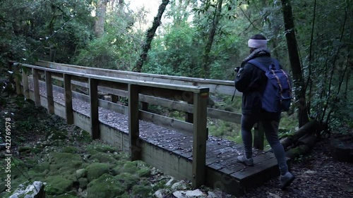 Girl crossing a wooden bridge surrounded by nature.