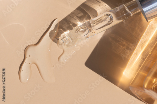 close up of pipette with pouring liquid serum with golden bottle and shadows photo