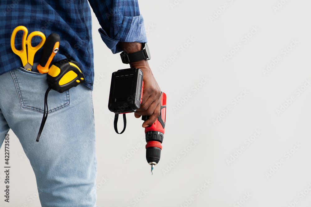 Black repairman holding electric drill in hand, in pocket measuring tape, screwdriver and scissors, copy space Black repairman holding electric drill in hand, in pocket measuring tape, screwdriver and scissors, copy space