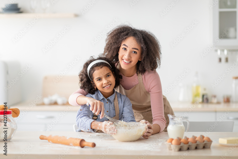 Positive black woman and daughter kneading dough in modern kitchen