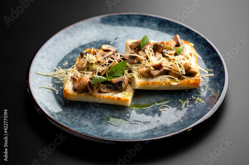 Bruschetta with mushrooms and tomatoes on a blue plate, on a black background.