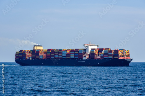 Fully loaded, large, cargo container ship sailing through the ocean. International transport of goods, including medical accessories and vaccine to fight Covid-19. 