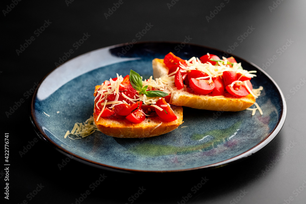 Bruschetta with mushrooms and tomatoes on a blue plate, on a black background.