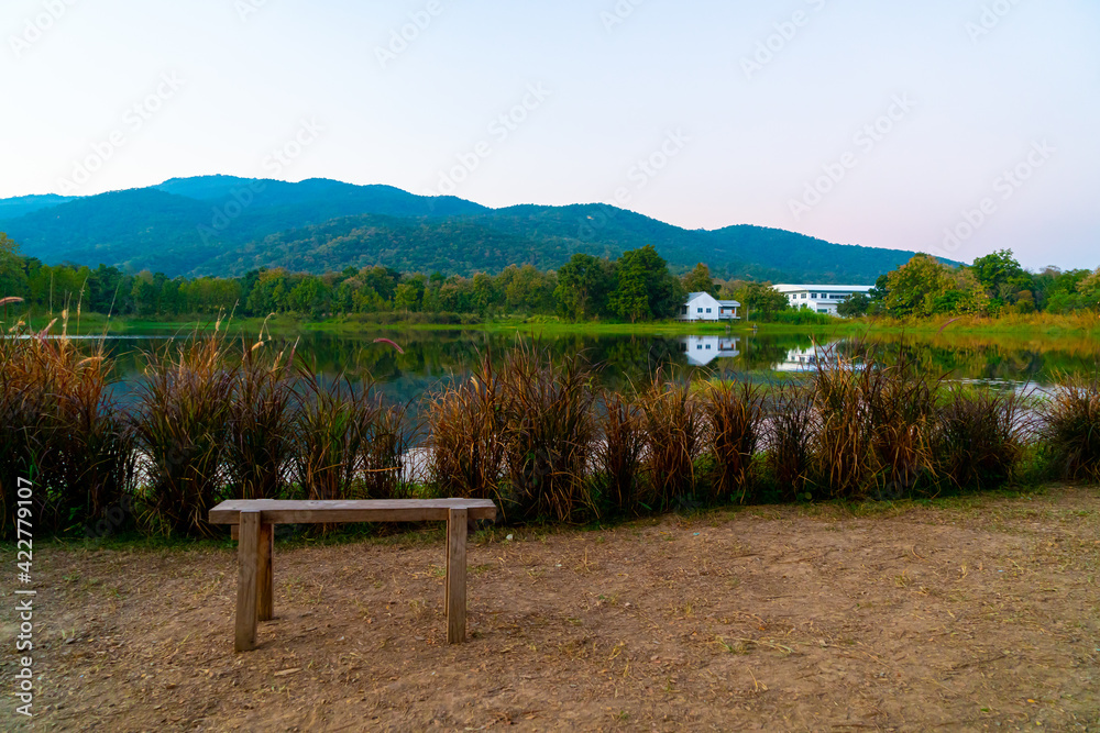 wood bench with beautiful lake at Chiang Mai with forested mountain and twilight sky