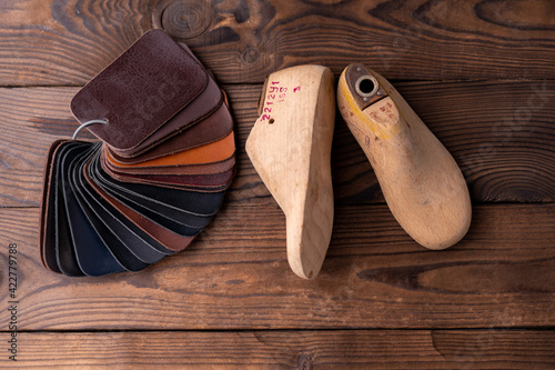 Leather samples for shoes and wooden shoe last on dark wooden table. Designer furniture clothes. Shoe maker workspace.