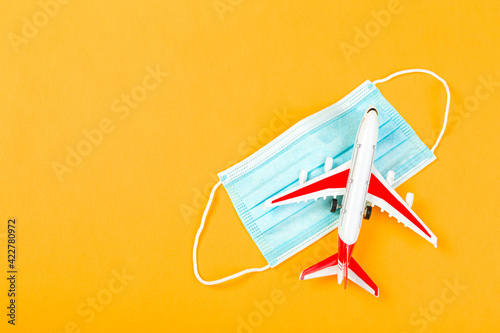 Airplane model with red wings with a blue medical mask. online ticketing and tourism concept during covid pandemic