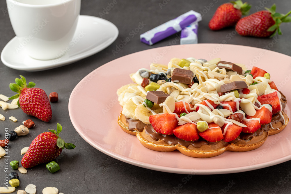 Heart waffle with banana and strawberry with gummy candy and ice cream on it.