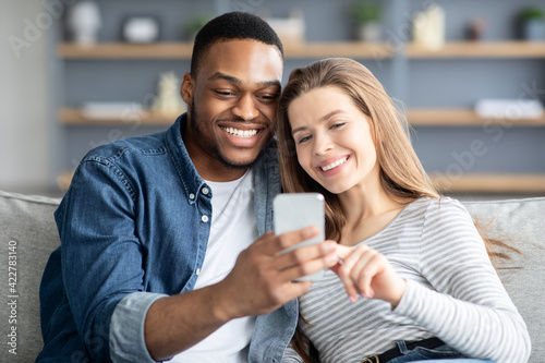 Cheerful mixed couple spending time with smartphone at home, watching videos