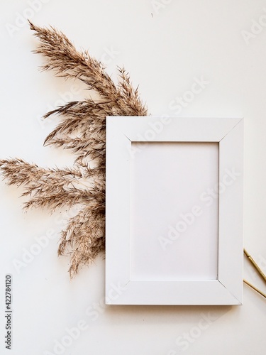 White frame mock up and dried natural pampas grass. Interior decoration element. Flatlay top view. Background boho. Minimalism design. Place for text. Selective focuson photo