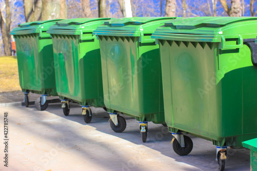Large green plastic trash cans on city street. Containers on wheels with a handle to collect commercial and resident trash. Disposal of household and industrial waste. Place for text.