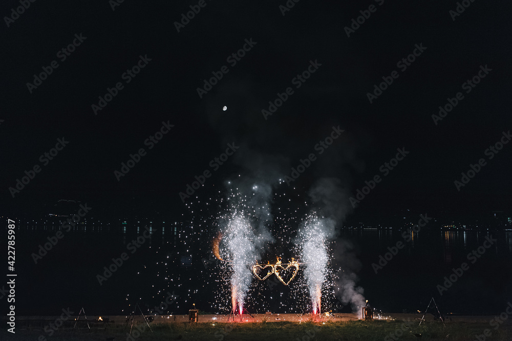 Beautiful and bright fireworks in nature on a festive day at a wedding. Burning heart, sparks, fire show decorations.