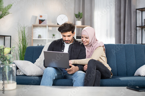 Happy young muslim couple using app on mobile phone at home
