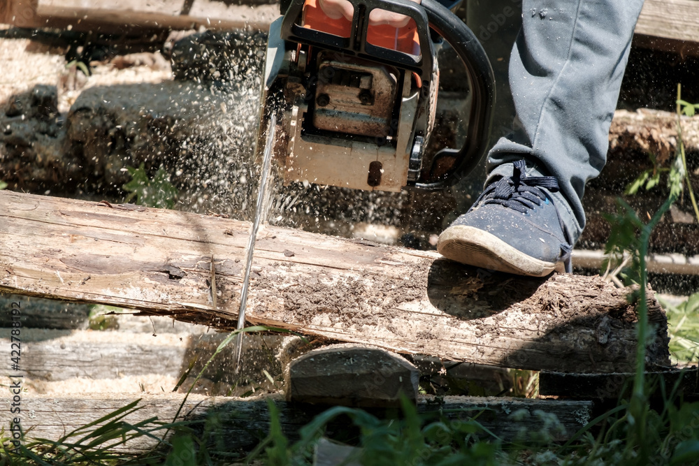 Male hands sawing old boards for firewood with a professional chainsaw, in a village yard. Winter preparation concept. Lifestyle. Male hands sawing old boards for firewood with a professional chainsaw, in a village yard. Winter preparation concept. Lifestyle.